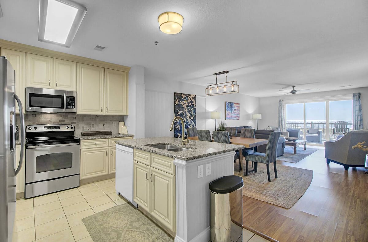 Open-concept kitchen with cream cabinets, granite countertop island, stainless steel appliances, and ocean view through living area
