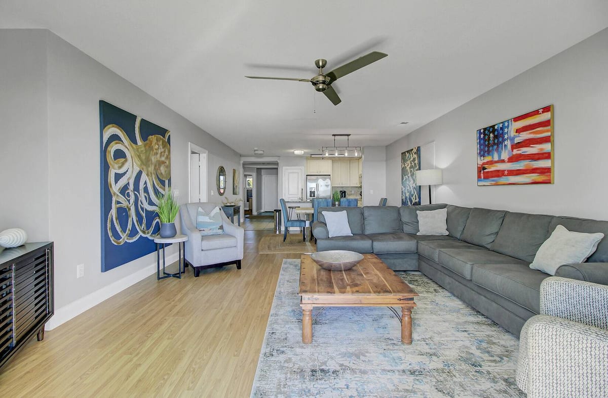 Wide-angle living room view showing open floor plan — octopus art, American flag painting, gray sectional, hardwood floors, and dining area beyond